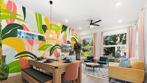 A modern living room with a wooden dining table, a sofa, and a large window with curtains. - *NEW* Pool table, fenced backyard, 1 mi to downtown, 5 mi to beach, 3BD/2BA (St. Augustine)
