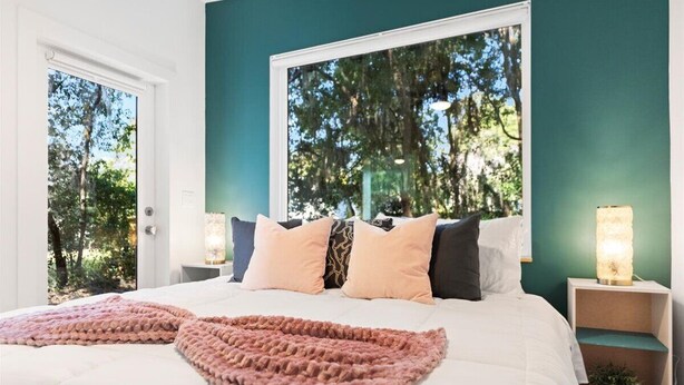 Un dormitorio con una cama grande, paredes color verde azulado y vistas a árboles a través de una ventana.
