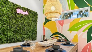 Un comedor con una pared verde, un mural abstracto y colorido, y una lámpara colgante.
