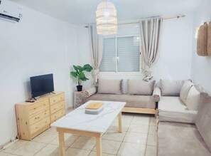 A living room with a sofa, a TV, a coffee table, a plant, and a window with curtains. - Nami's House (TETOUAN)