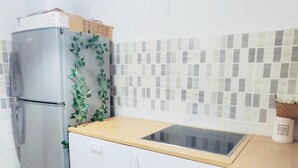 Eine kleine Küche mit Kühlschrank, Mikrowelle, Spüle und einer gefliesten Spritzschutzwand.