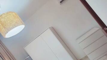 Una habitación con un armario blanco, una lámpara colgante y aire acondicionado instalado en la pared.