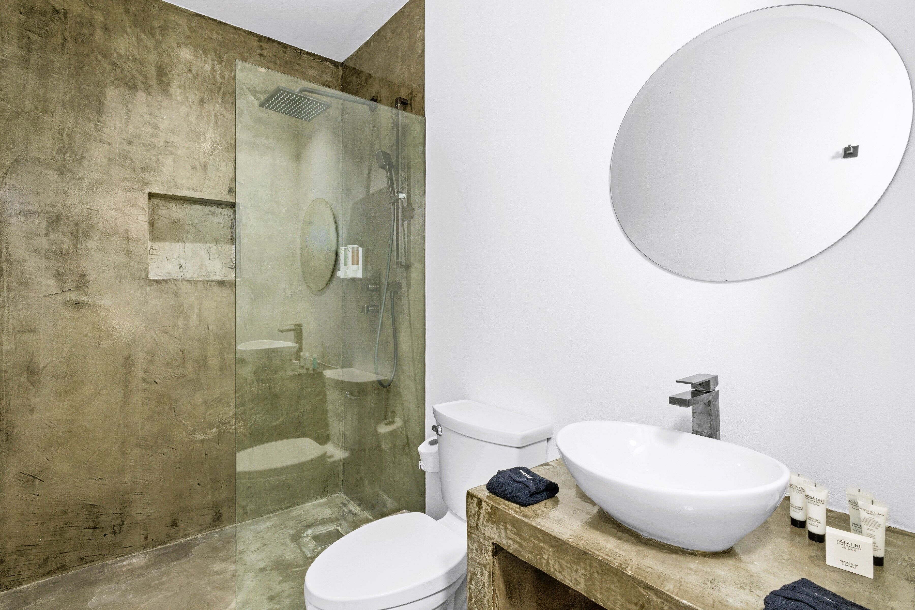Un bagno con doccia vetrata, un water bianco, un mobiletto in legno con un lavandino ampio e bianco e uno specchio rotondo.