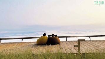 Dos personas sentadas sobre grandes objetos redondos y con forma de asiento en una terraza de madera con vista a las nubes.
