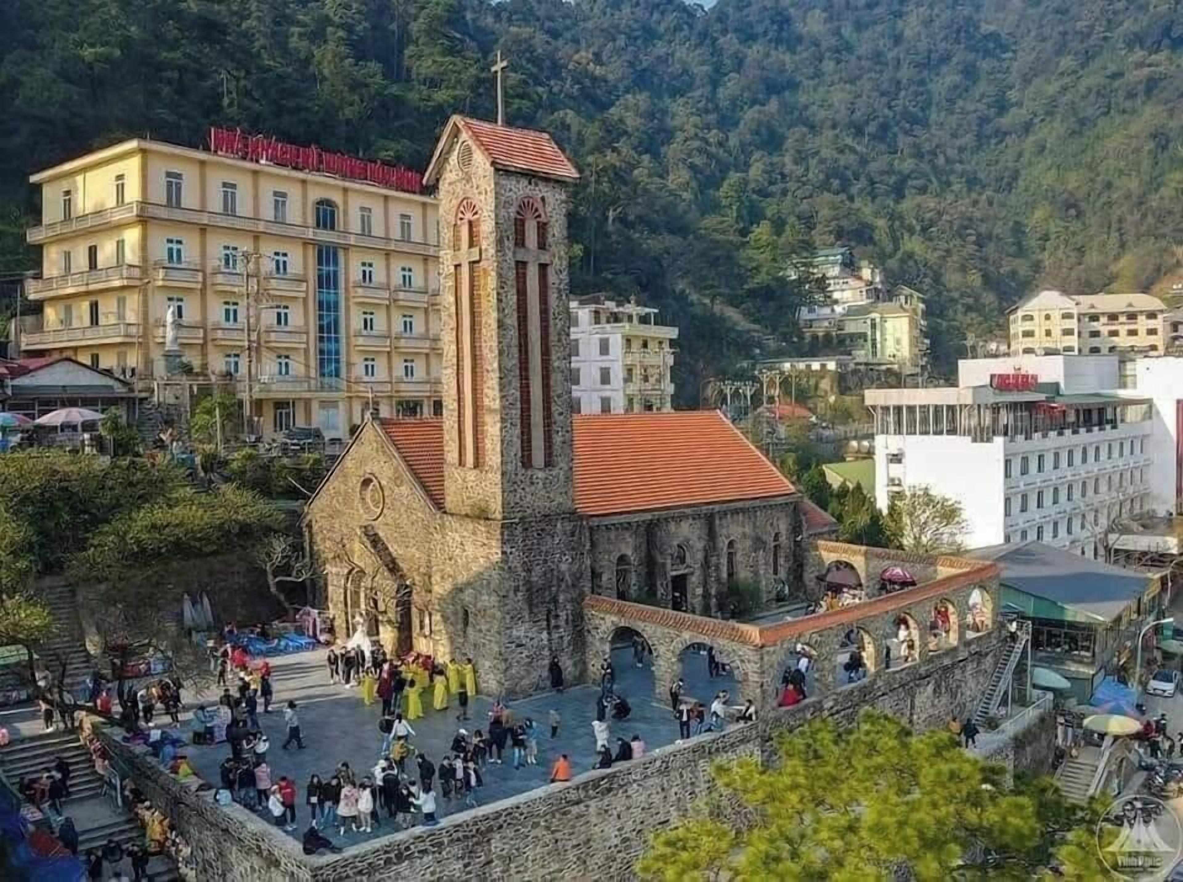 A historic church with a bell tower, surrounded by a stone wall and a crowd of people.
