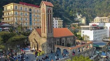 Una iglesia histórica con un campanario, rodeada por un muro de piedra y una multitud de gente.