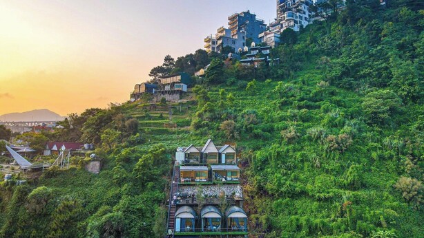 A hillside hotel with multiple buildings, including a prominent structure with a unique architectural design featuring arched windows and balconies. - Ngan Ha Hotel Panorama View (Tam Dao)