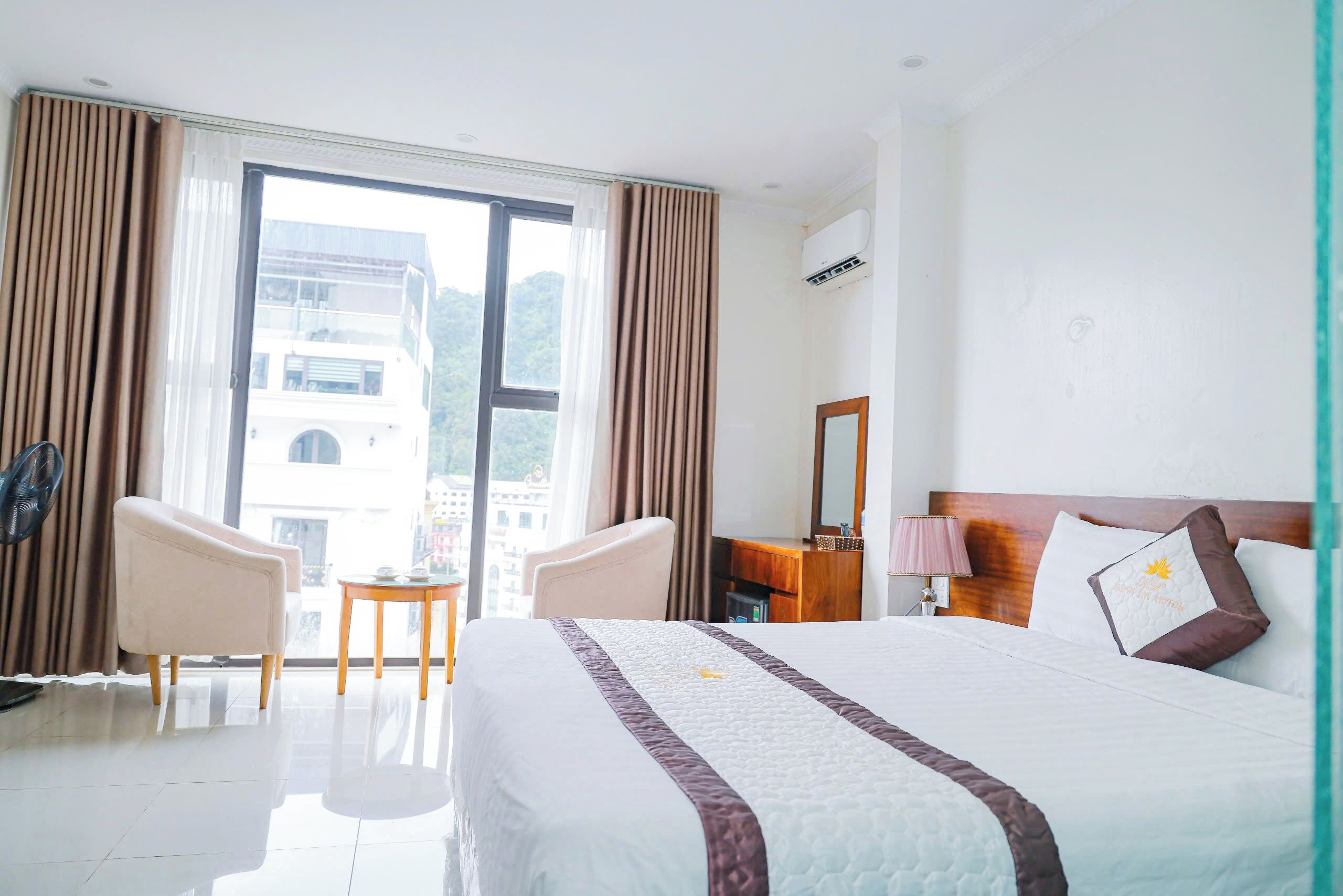 Habitación de hotel con cama, dos sillas, una mesita, escritorio, espejo y ventana con cortinas.