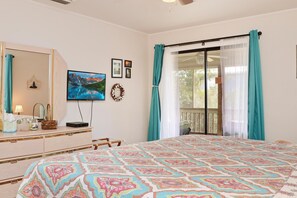 A bedroom with a large bed, a dresser, a television, and a window with curtains. - Blue Moon Cottage (Port St. Joe)