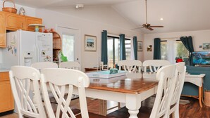 Un coin repas avec une table en bois et des chaises blanches, une cuisine avec des meubles en bois et un ventilateur de plafond.