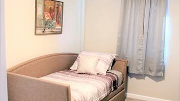A bedroom with a single bed, a ceiling fan, a window with curtains, and a painting on the wall.