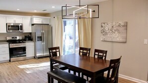 A modern kitchen with white cabinets, stainless steel appliances, and a wooden dining table with chairs. - Guesthouse 3BDR Suite (Overland Park)