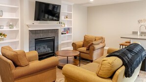 A modern living room with a fireplace, a flat-screen TV, and a kitchen area. - Guesthouse 3BDR Suite (Overland Park)