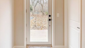 A hallway with a wooden floor, a white door with a glass panel, and a patterned doormat. - Guesthouse 3BDR Suite (Overland Park)