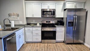 A modern kitchen with white cabinets, stainless steel appliances, and a wooden floor. - Guesthouse 3BDR Suite (Overland Park)