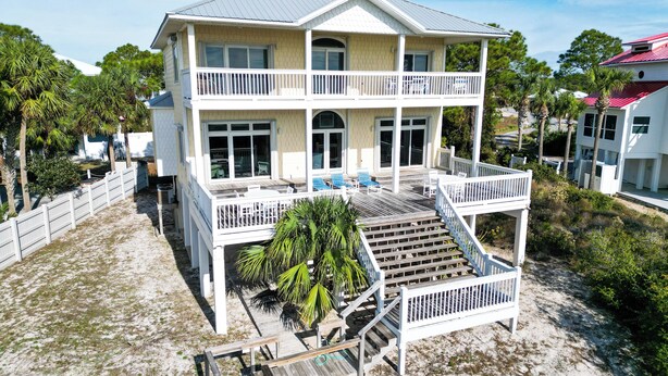 Une maison à deux étages située en bord de mer, dotée d’un balcon, d’une terrasse couverte et d’un escalier menant à l’étage supérieur.