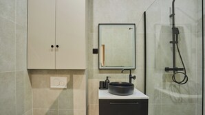 A modern bathroom with a large mirror, a black sink, and a shower enclosure.