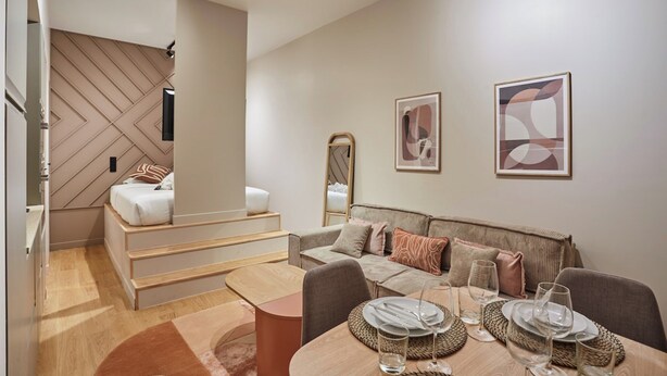 A modern, well-lit room with a bed, a sofa, and a dining area with a table set for two.