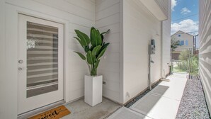 En hvid facade med en dør, en potteplante og en dørmåtte.