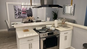 Una cucina moderna con mobili bianchi, un piano cottura in acciaio inossidabile e un grande specchio sopra il bancone.