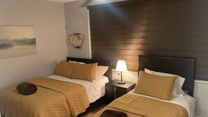 Una camera d'albergo con due letti, ciascuno con copripiumino e cuscini marroni, un comodino con una lampada e un'opera d'arte appesa al muro.