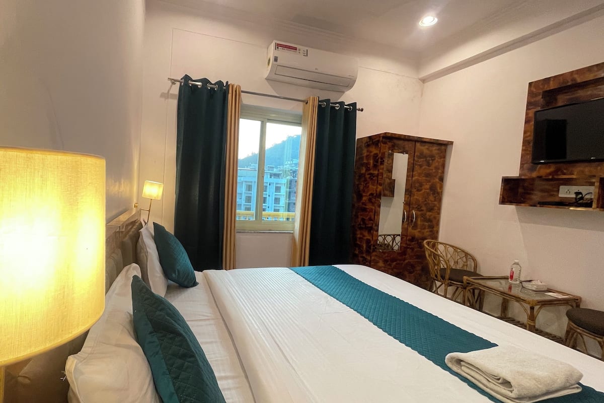 A hotel room with a bed, a lamp, a TV, and a window with curtains.
