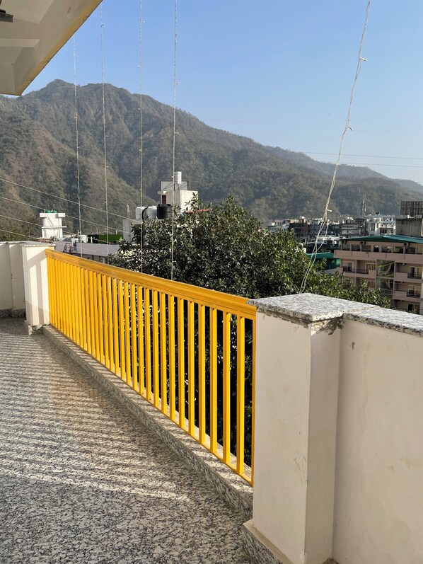 A balcony with a yellow railing overlooking a cityscape with buildings and a mountain in the background. - GreenDay Escapes (Rishikesh)