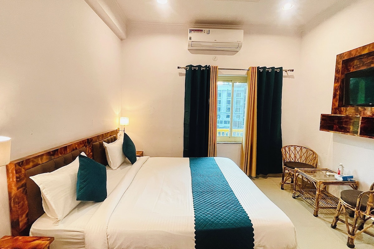 A hotel room with a bed, a TV mounted on the wall, a chair, and a window with curtains.