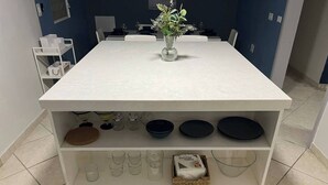 A kitchen with a white countertop, a vase with flowers, and shelves holding various kitchenware. - Kasa Metropolios 4-bedroom house w AC, WiFi, 2 car garage 7 minutes from airport (Carolina)