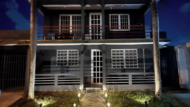 A two-story building with a balcony, large windows, and a gated entrance. - Kasa Metropolios 4-bedroom house w AC, WiFi, 2 car garage 7 minutes from airport (Carolina)