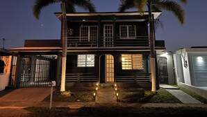 A two-story house with a balcony, a gated entrance, and a well-lit front yard with a pathway. - Kasa Metropolios 4-bedroom house w AC, WiFi, 2 car garage 7 minutes from airport (Carolina)