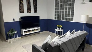 A living room with a TV, sofa, and decorative items. - Kasa Metropolios 4-bedroom house w AC, WiFi, 2 car garage 7 minutes from airport (Carolina)