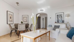 Ένα μοντέρνο σαλόνι με τραπεζαρία, έναν λευκό καναπέ, ένα τραπεζάκι σαλονιού και έργα τέχνης σε κορνίζες στους τοίχους.
