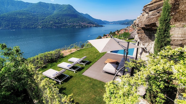 Une propriété située au bord du lac, dotée d’une piscine, de chaises longues et offrant une vue sur le lac et les montagnes.