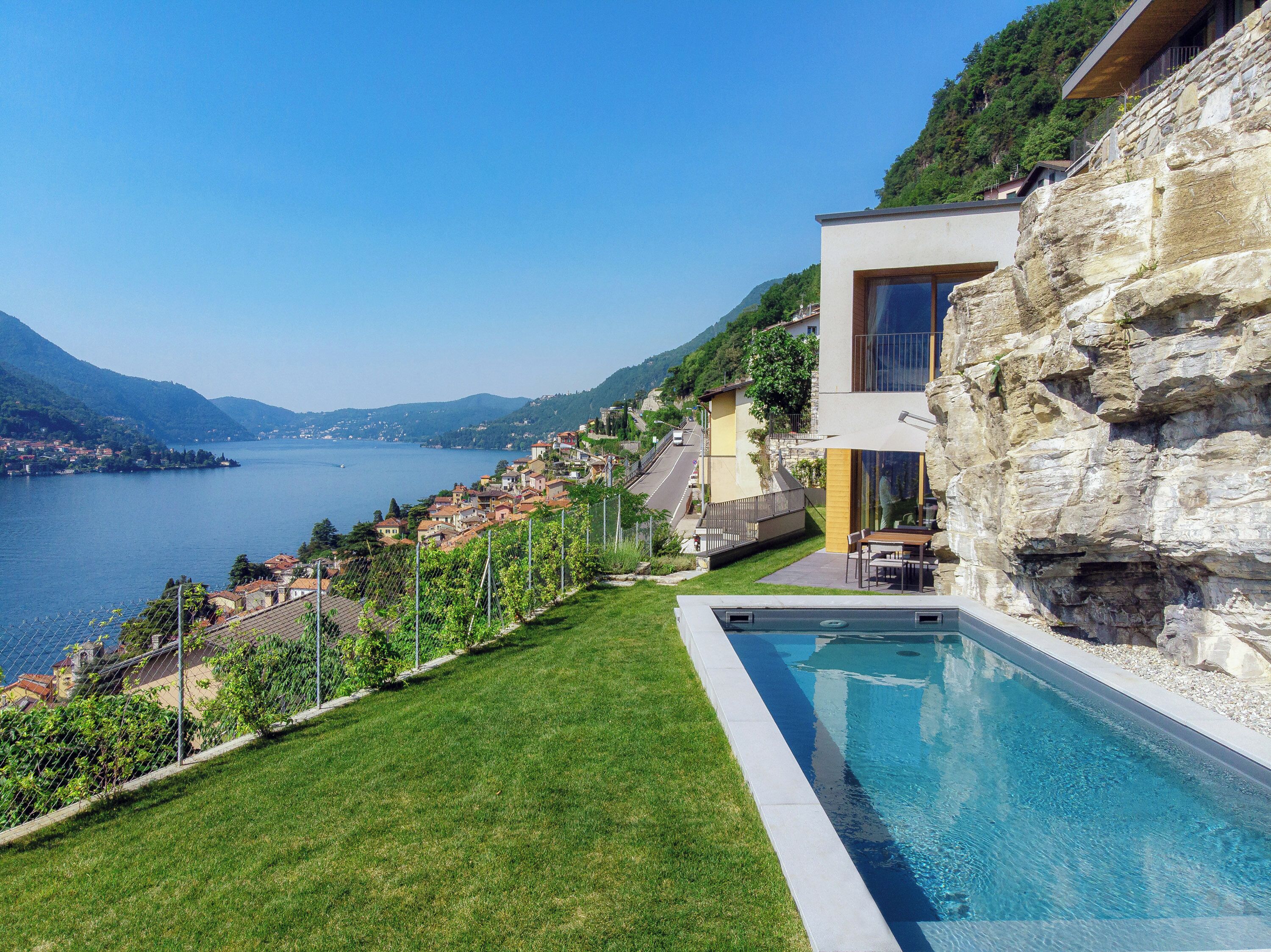 A modern house with a pool, a view of a lake, and a hillside with buildings.