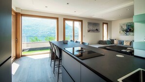 Une cuisine moderne dotée d’un grand îlot central, d’un coin repas avec des chaises et d’une vue sur les montagnes grâce à de grandes fenêtres.