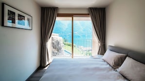 Une chambre d’hôtel avec un grand lit, une vue sur les montagnes et un plan d’eau visible par une porte coulissante, ainsi qu’une photo encadrée accrochée au mur.