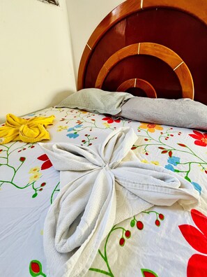Ein ordentlich bezogenes Bett mit einer blumigen Tagesdecke, einem gefalteten Handtuch und einem gelben Handtuch daneben.