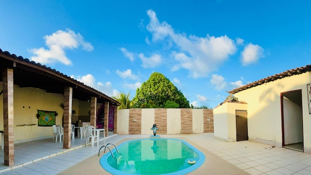 A swimming pool with a tiled deck, surrounded by a covered patio area with chairs and a table. - Harmô Hostel Cultural (Conde)