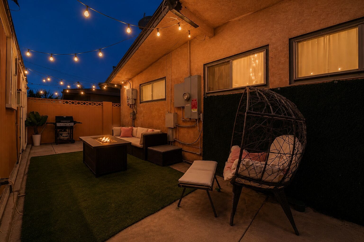 An outdoor patio with a fire pit, seating, and string lights.
