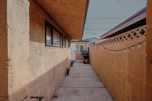 A narrow concrete pathway flanked by brick walls, leading to a door with a small garden area. - Private 2 Bedroom Guesthouse Near Fremont! (Las Vegas)