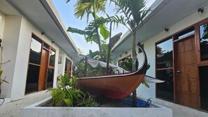 A boat-shaped planter in a courtyard with potted plants and a building with large windows and a door. - Dhontakuru Guesthouse (Dhidhdhoo)