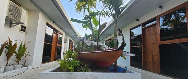 A boat-shaped planter in a courtyard with potted plants and a building with large windows and a door. - Dhontakuru Guesthouse (Dhidhdhoo)