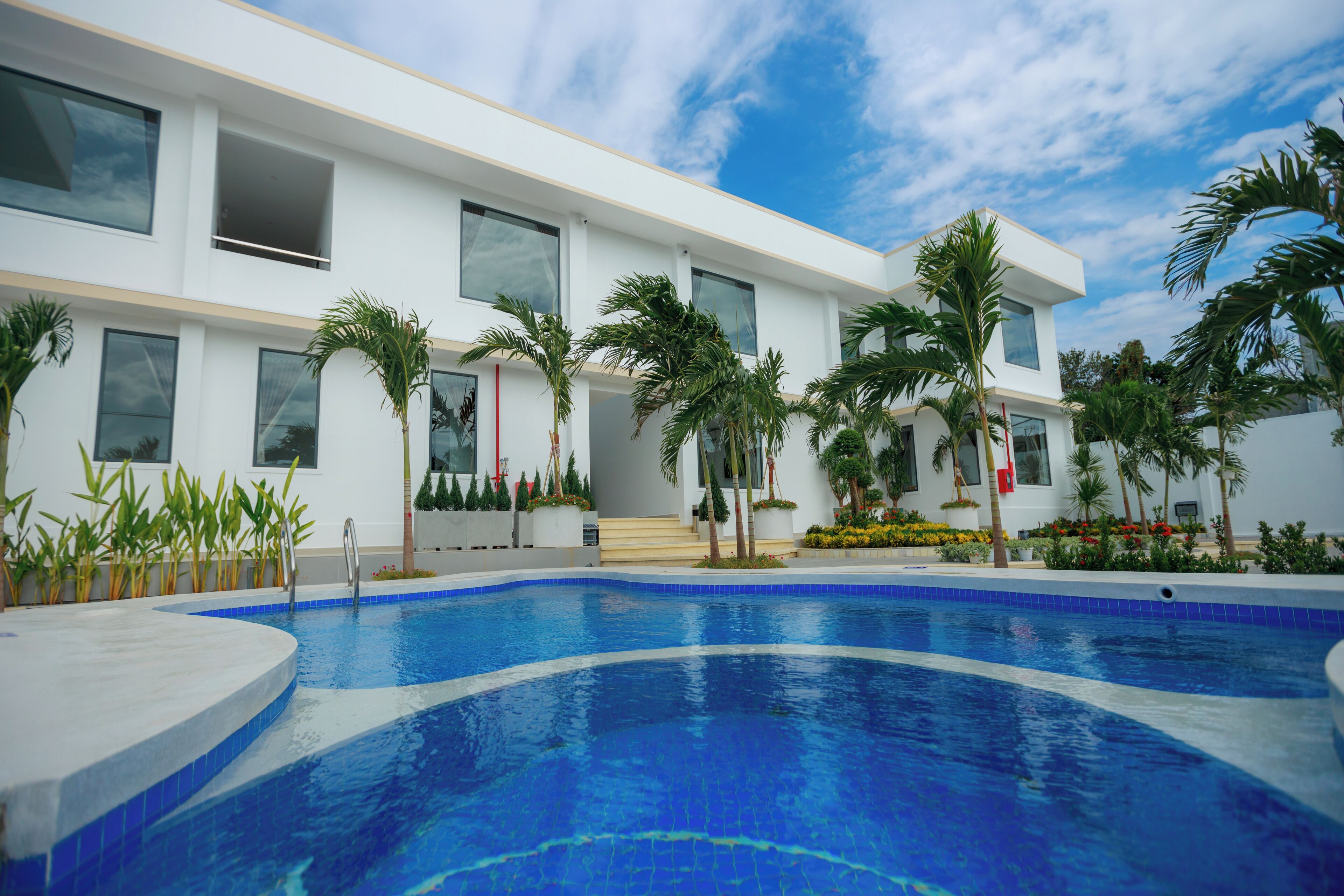 A modern building with a swimming pool, surrounded by palm trees and plants.