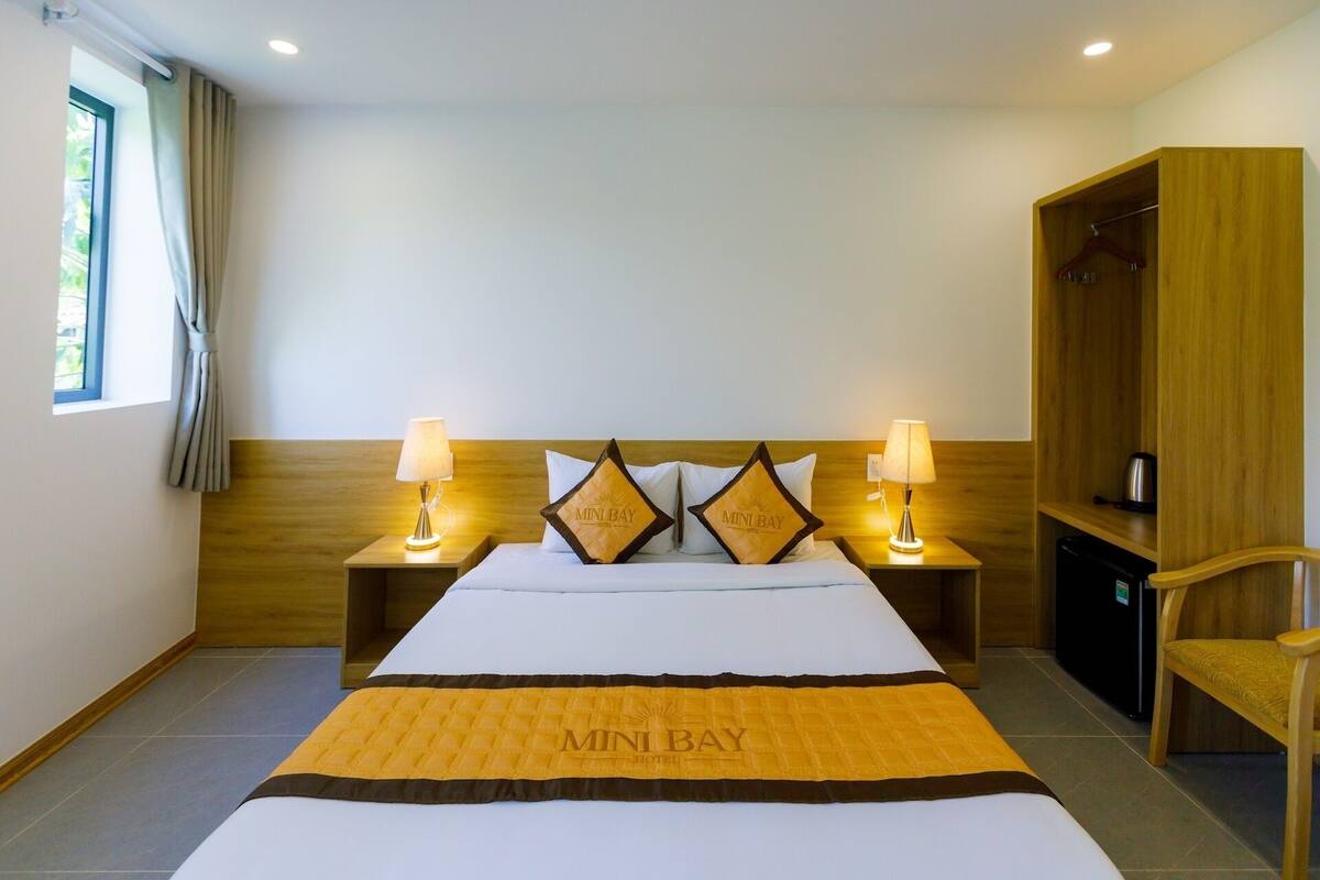 A hotel room with a bed, two bedside lamps, a wardrobe, and a window with curtains.
