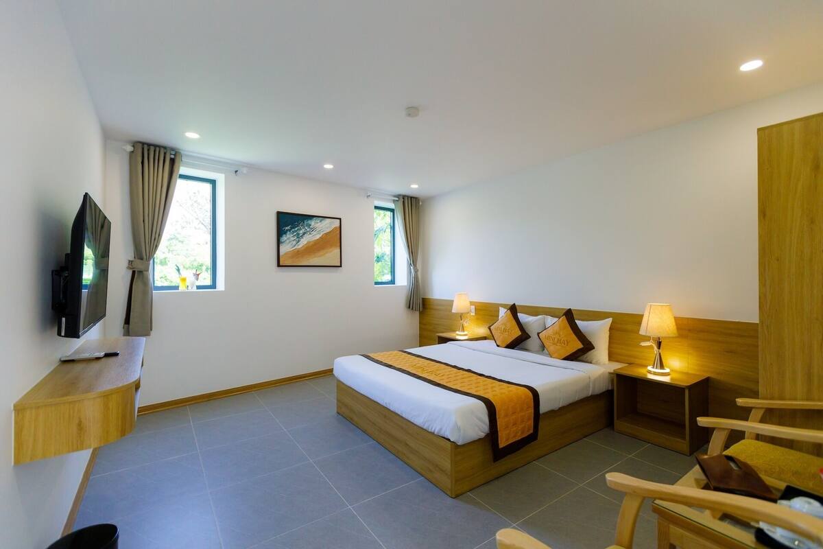 A hotel room with a bed, bedside tables, a TV, and a painting.