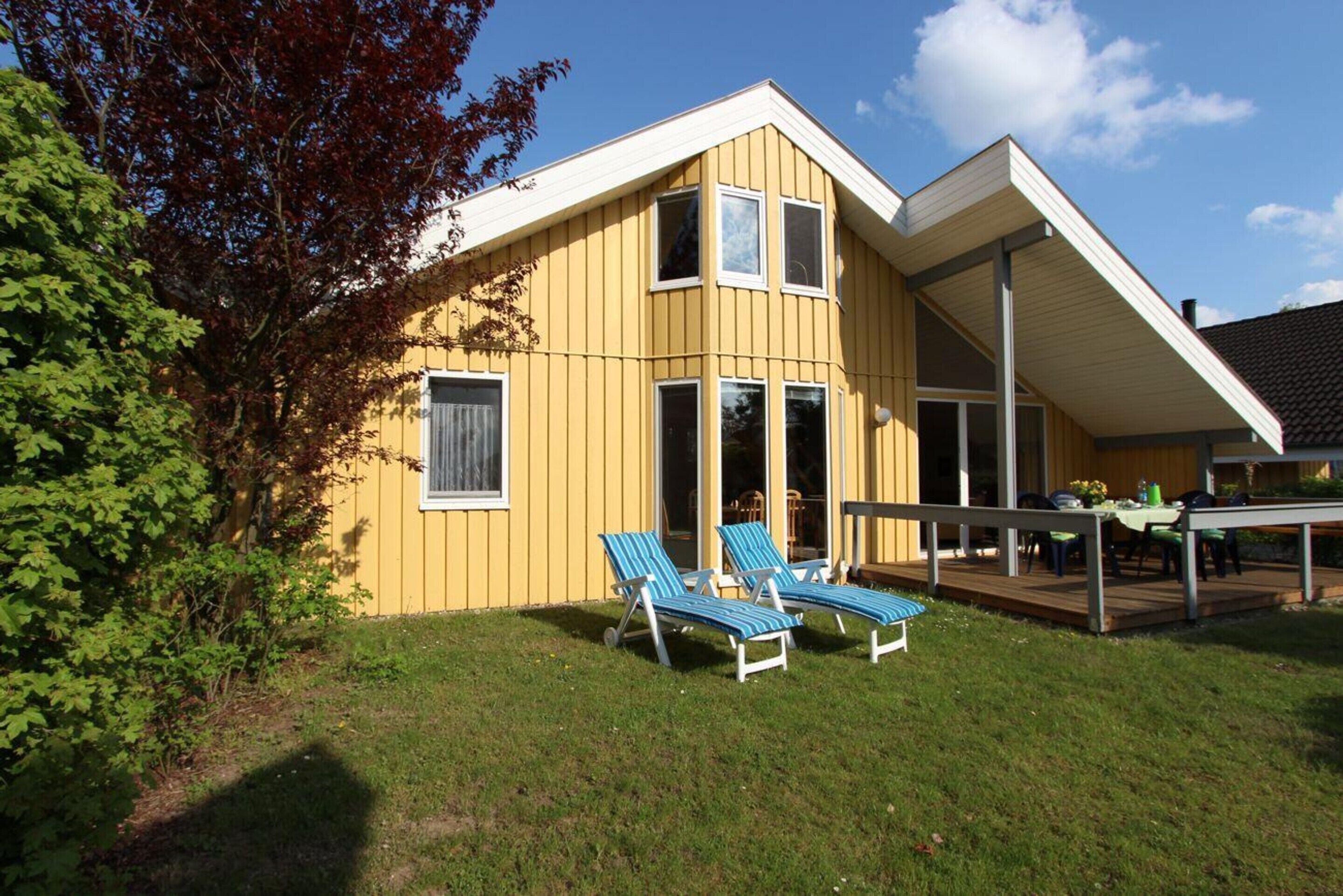 A yellow building with a deck, two lounge chairs, and a table with chairs.