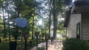 A wooden deck leading to a house with a metal railing, surrounded by trees and potted plants.