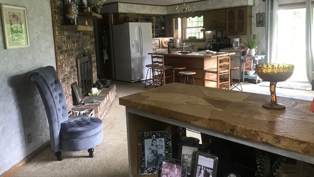 A kitchen with a refrigerator, stove, and dining area. There is a blue chair and a wooden table.
