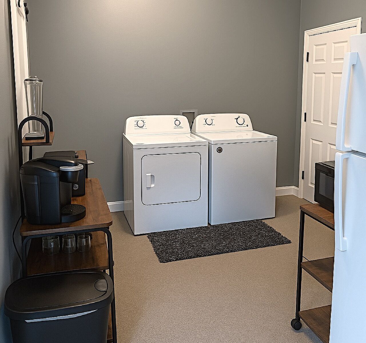 A laundry room with two stacked washers and dryers, a coffee maker, and a small table with glasses.